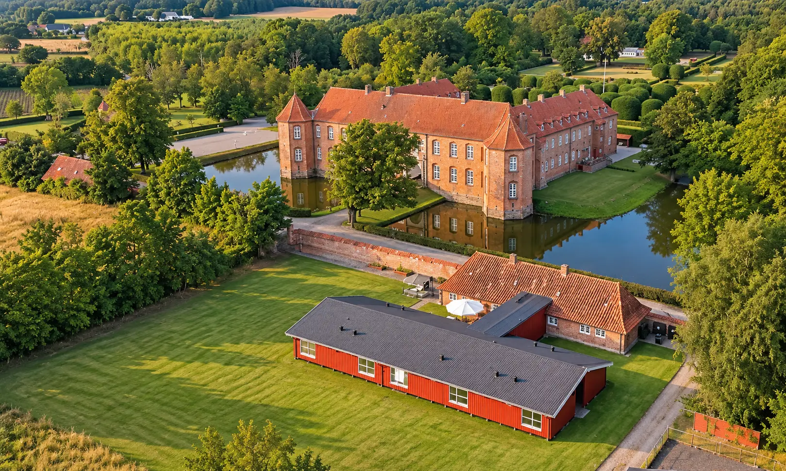 Luftfoto af Hotel Møllehusets lange røde bygning foran Visborggaard Slot, voldgraven og de grønne omgivelser